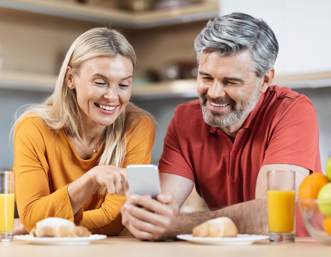 A smiling couple at their kitchen counter, looking at a phone together